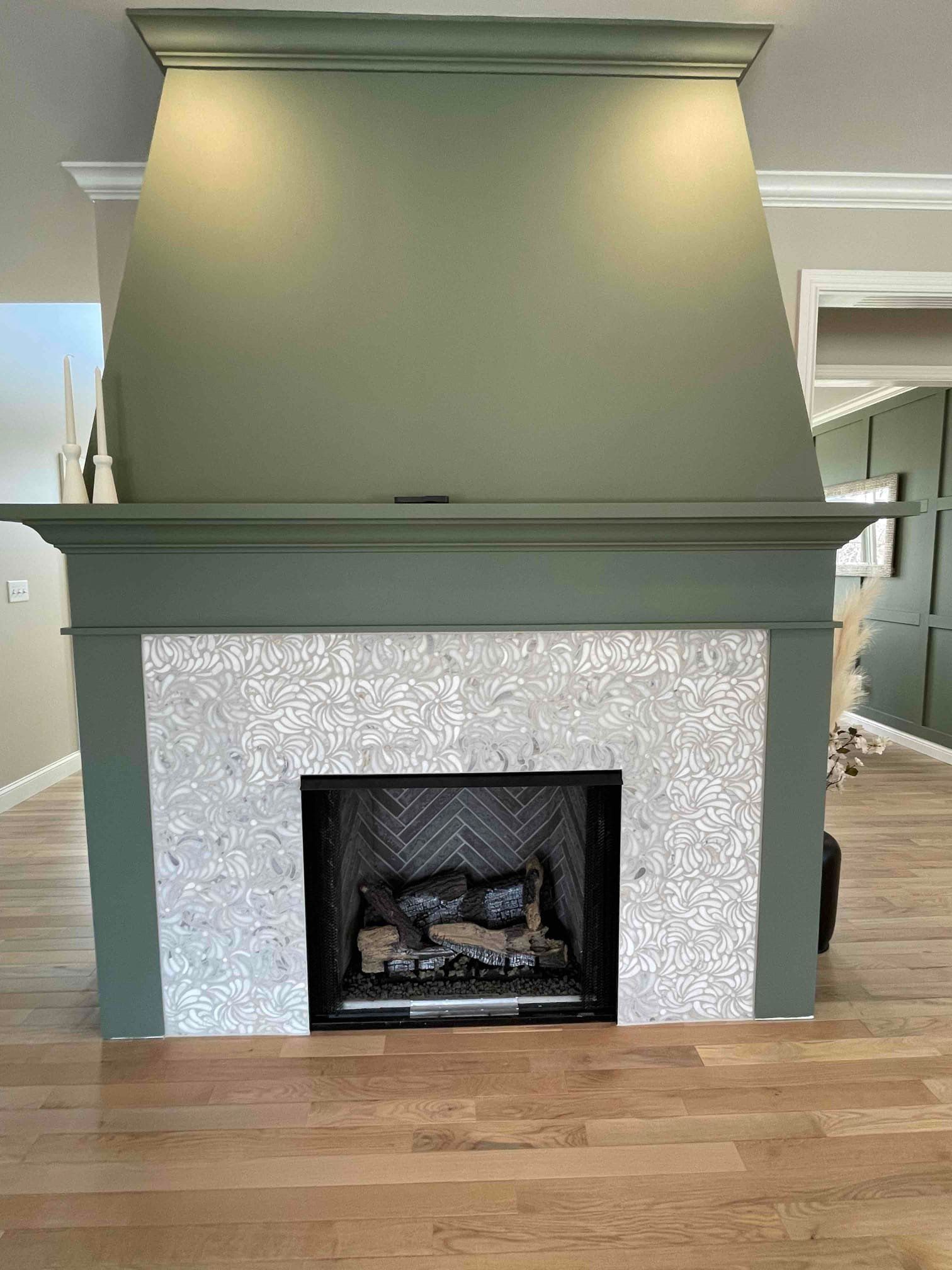 Sage green fireplace surround with a tapered custom hood, white relief tile and a herringbone firebox