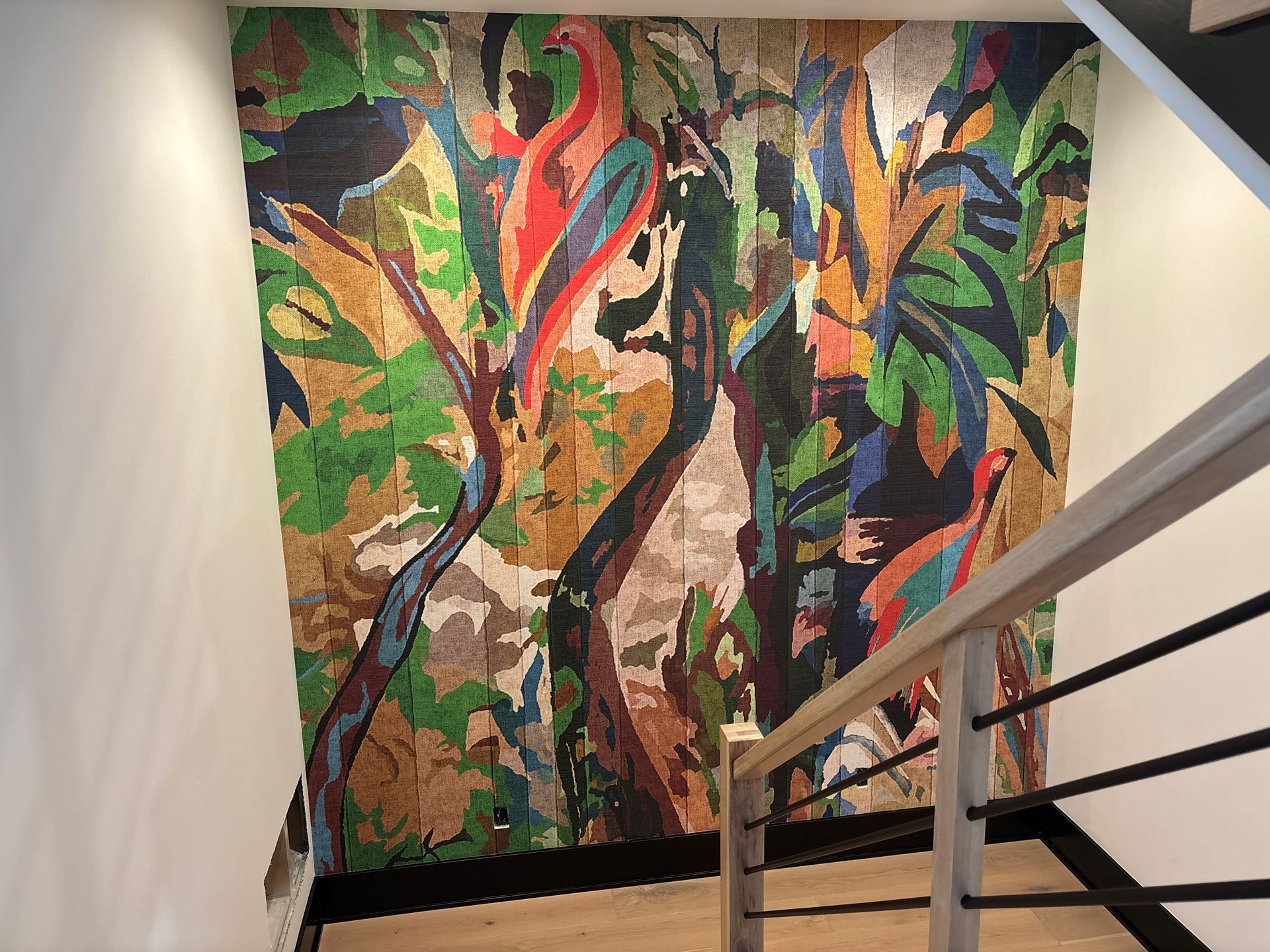 Stairwell wall covered in a bold tropical bird mural wallpaper beside a pale oak handrail